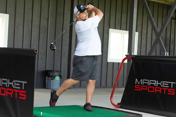 A man takes a swing on the artificial turf driving range mats.